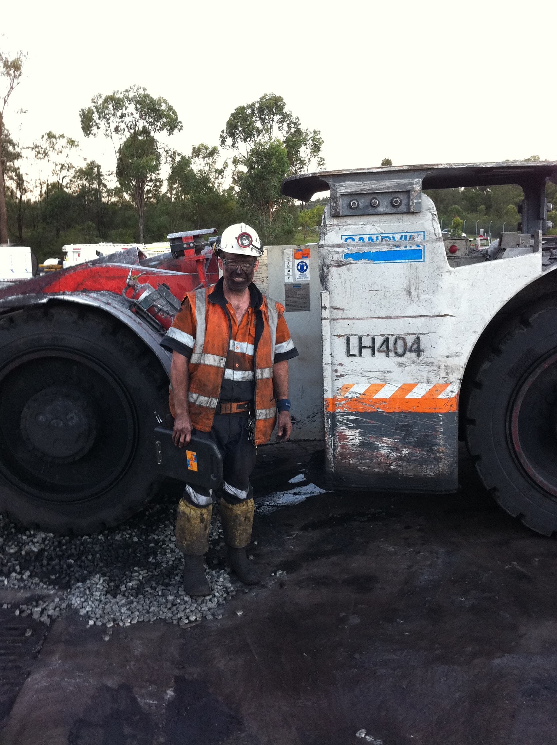 A coal-dusted roof bolter in hi-vis standing in front of an underground loader at the end of a shift