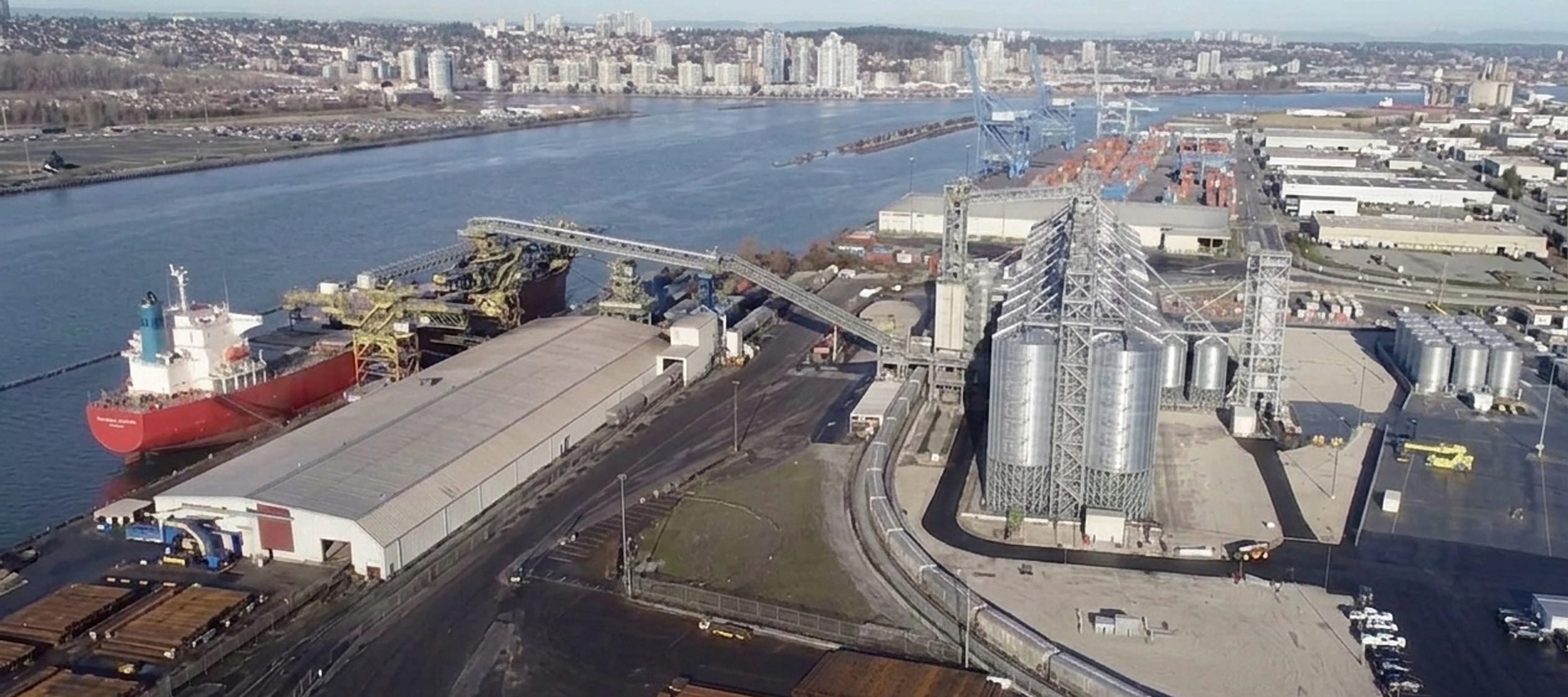 Aerial view of the grain terminal — silos, rail loop and berthed bulk carrier on the working harbour